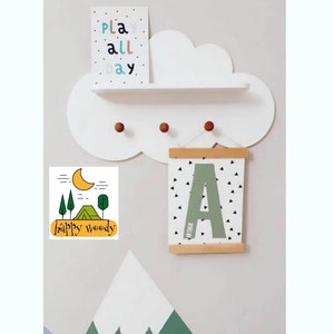 Könnte beinhalten: Ein weißes, wolkenförmiges Regal mit drei Holzgriffen, einem kleinen Schild mit der Aufschrift "play all day" und einem gerahmten Druck mit dem Buchstaben "A" und schwarzen Dreiecken auf weißem Hintergrund. Der Druck hängt an einer Holzleiste. Unter dem Regal befindet sich ein grünes und weißes Wandtattoo in Form eines Berges.