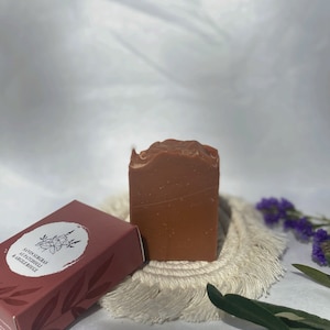 Peut inclure: Un savon rouge-brun avec une étiquette blanche qui indique "Savonsiers  d'Patchouli & Argile Rouge".