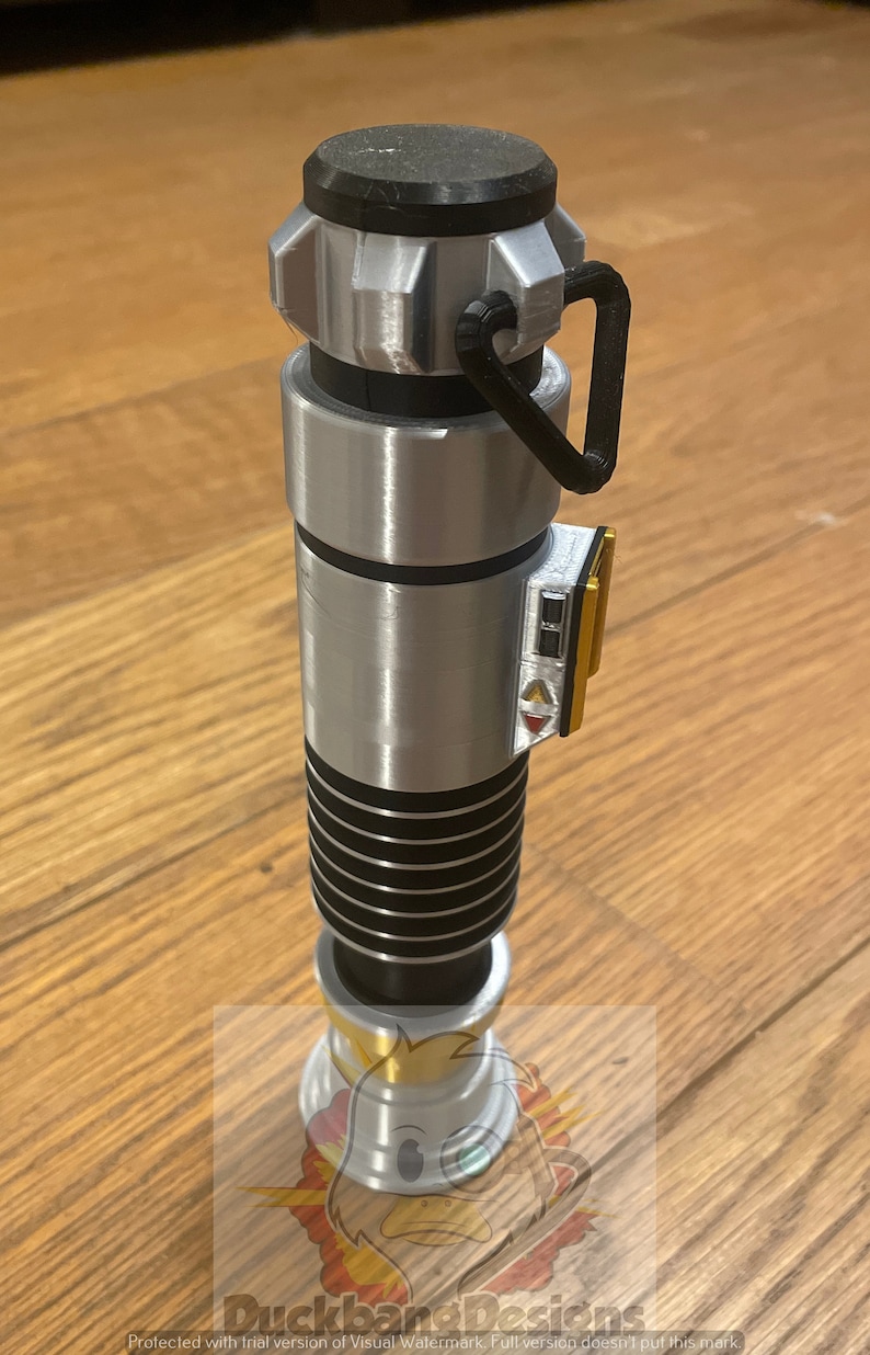 May include: A silver and black lightsaber with a black handle and a gold accent. The lightsaber has a black and silver grip and a black and silver blade.