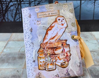May include: A vintage-style journal with a white owl perched on a stack of books. The cover features a lace trim, burlap, and the words "School of Magic".