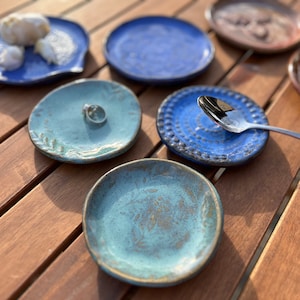 May include: A set of six ceramic dishes in various shades of blue and green. The dishes are all round and have a slightly textured surface. Some of the dishes have a decorative design, while others are plain. The dishes are perfect for serving small snacks or appetizers.
