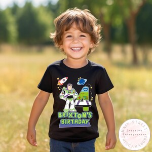 K&ouml;nnte beinhalten: Schwarzes T-Shirt mit einer bunten Grafik von Buzz Lightyear, einer Rakete und einem Planeten. Das Shirt enth&auml;lt den Text "Brixton's Birthday" und die Zahl 4. Das Shirt wird von einem Kind getragen.