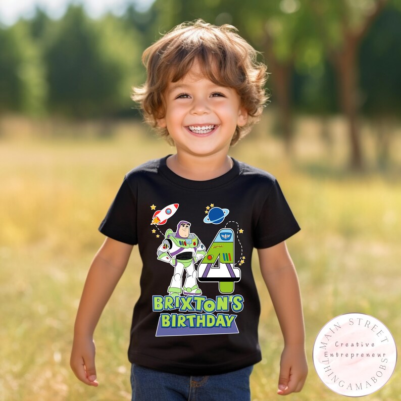 K&ouml;nnte beinhalten: Schwarzes T-Shirt mit einer bunten Grafik von Buzz Lightyear, einer Rakete und einem Planeten. Das Shirt enth&auml;lt den Text "Brixton's Birthday" und die Zahl 4. Das Shirt wird von einem Kind getragen.