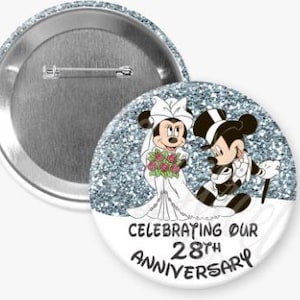 May include: A round button with a silver metal back and a cartoon image of Mickey and Minnie Mouse dressed as a bride and groom. The button has a glittery blue background and text that reads "Celebrating Our 28th Anniversary."