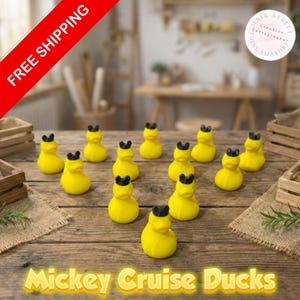 May include: A collection of yellow rubber ducks with black ears, arranged on a wooden surface. The ducks are labeled "Mickey Cruise Ducks". The background includes wooden crates and a blurred interior setting.