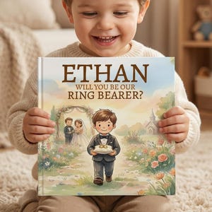May include: A personalized children's book with the name "ETHAN" in large, brown letters. The book's title reads "WILL YOU BE OUR RING BEARER?" with an illustration of a wedding scene. The book is held by a smiling child.