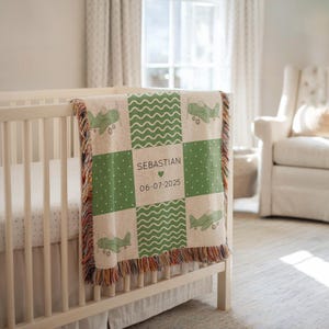 以下が含まれることがあります： ベビーベッドに掛けられたパーソナライズされたベビーブランケット。ブランケットは、緑色の正方形、飛行機、波模様のパッチワークデザインが特徴です。「Sebastian」という名前、ハート、日付「06-07-2025」が表示されています。ブランケットにはフリンジエッジが付いています。