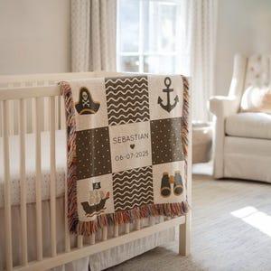 May include: A beige and brown pirate-themed baby blanket with a fringe. The blanket features a pirate hat, anchor, ship, and binoculars. The name "Sebastian" and the date "06-07-2025" are also displayed on the blanket.