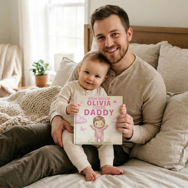 Peut inclure: Un livre pour enfants personnalis&eacute; intitul&eacute; &laquo;&nbsp;How Much Olivia loves Daddy&nbsp;&raquo;. La couverture pr&eacute;sente une illustration de b&eacute;b&eacute; en rose, avec des nuages et des c&oelig;urs roses. Le livre est tenu par un b&eacute;b&eacute; et un homme.
