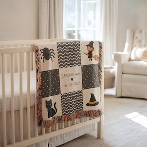 Pode incluir: Um cobertor de bebê com tema de Halloween bege e cinza com um design de gato preto, aranha, bruxa e chapéu de bruxa. O cobertor é personalizado com o nome "Sebastian" e a data "06-07-2025".