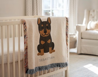 Puede incluir: Una manta beige con un diseño de perro de dibujos animados en negro y marrón, sobre una cuna blanca. La manta tiene un borde con flecos con hilos coloridos y el nombre "SEBASTIAN" está impreso.