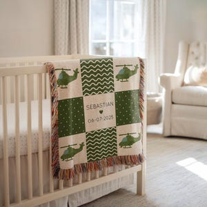 May include: A personalized baby blanket with a green helicopter design, displayed on a white crib. The blanket features the name "Sebastian" and the date "06-07-2025". The design includes green polka dots and wavy lines.