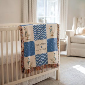 May include: A personalized baby blanket with a patchwork design. The blanket features squares of blue polka dots, wavy lines, and images of geese wearing hats and scarves. The center square displays the name "Sebastian" and the date "06-07-2025".