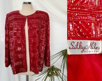 Può includere: Un cardigan rosso con paillettes e un motivo geometrico. Il cardigan ha maniche lunghe e un'apertura frontale. L'etichetta recita "Silky Nites NEW YORK".