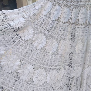 May include: White crocheted tablecloth with a delicate floral pattern. The tablecloth is made of fine thread and has a delicate, lacy appearance.