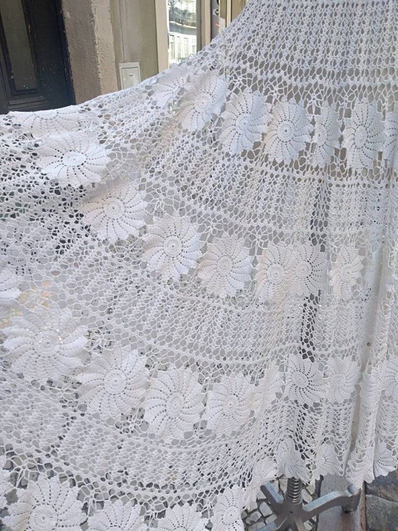 May include: White crocheted tablecloth with a delicate floral pattern. The tablecloth is made of fine thread and has a delicate, lacy appearance.