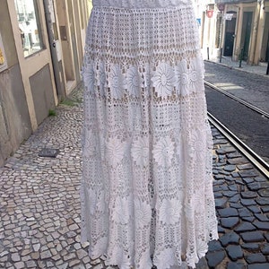 May include: A white crochet skirt with a scalloped hem and floral details. The skirt is made of delicate lace and has a flowing silhouette.