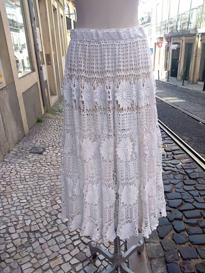 May include: A white crochet skirt with a scalloped hem and floral details. The skirt is made of delicate lace and has a flowing silhouette.