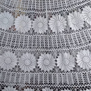 May include: White crocheted tablecloth with a delicate floral pattern. The tablecloth features a repeating design of small, intricate flowers.