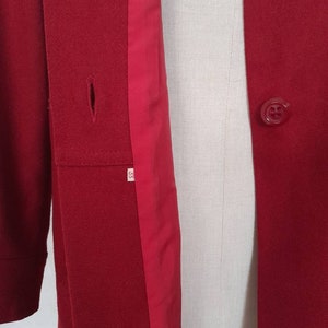 K&ouml;nnte beinhalten: Ein roter Wollmantel mit rotem Futter und einem einzigen Knopfverschluss. Der Mantel hat einen kleinen Riss auf der linken Seite.