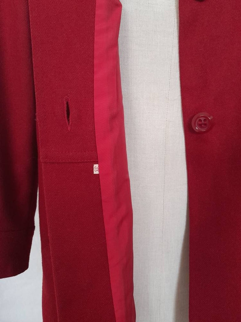 K&ouml;nnte beinhalten: Ein roter Wollmantel mit rotem Futter und einem einzigen Knopfverschluss. Der Mantel hat einen kleinen Riss auf der linken Seite.