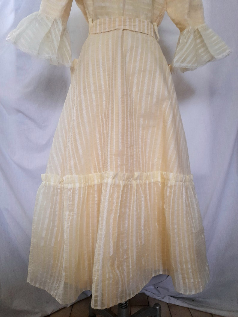 May include: A yellow, sheer dress with a striped pattern and a ruffled hem. The dress has a fitted bodice and a full skirt.