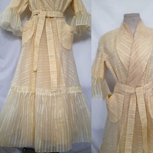 May include: A pale yellow sheer robe with a striped pattern, long sleeves with ruffled cuffs, and a matching sash tie. The robe has two patch pockets and a ruffled hem.