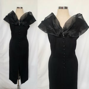 May include: A black sleeveless dress with a sheer black overlay collar and a row of buttons down the front.