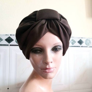 May include: A brown turban with a square knot on top. The turban is made of a soft, stretchy fabric.