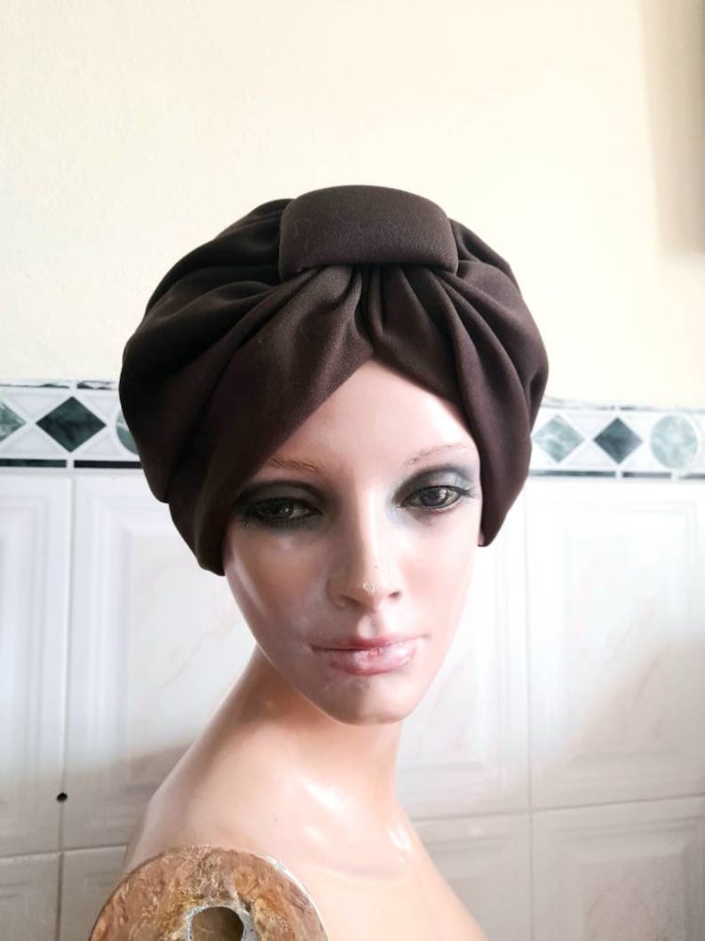 May include: A brown turban with a square knot on top. The turban is made of a soft, stretchy fabric.