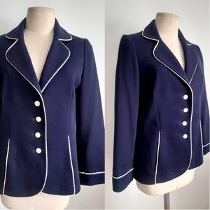 May include: A navy blue blazer with white piping around the collar, cuffs, and edges. The blazer has a button closure and four buttons down the front.