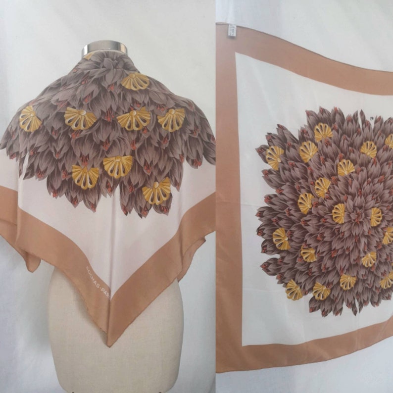 May include: A white silk scarf with a brown and gold floral design. The scarf has a brown border and the text "Christian Dior" is printed in the lower corner.