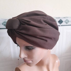 May include: A brown turban style head covering with a knotted detail on top.