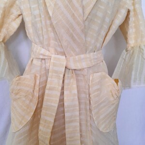 May include: A sheer, cream-colored robe with a striped pattern and a tie belt. The robe has two patch pockets on the front.