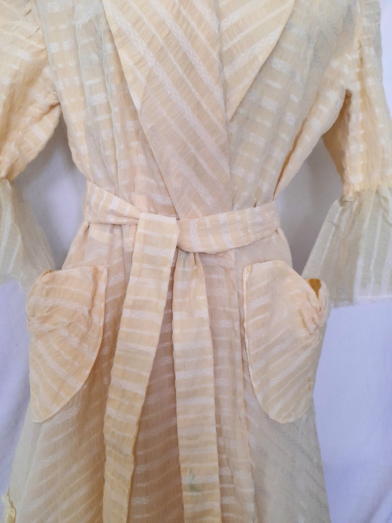 May include: A sheer, cream-colored robe with a striped pattern and a tie belt. The robe has two patch pockets on the front.