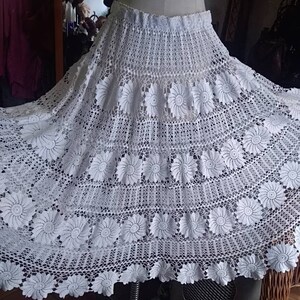 May include: A white crocheted skirt with a floral design. The skirt is full and flowing, and it has a scalloped hem.