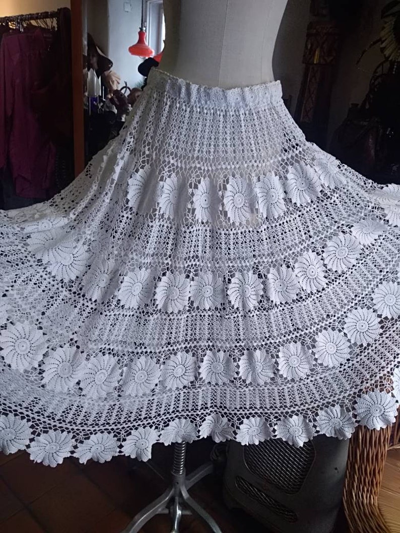 May include: A white crocheted skirt with a floral design. The skirt is full and flowing, and it has a scalloped hem.