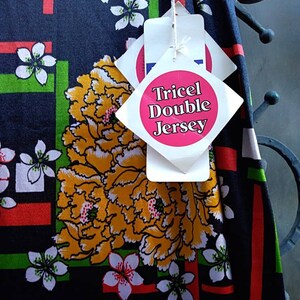 Pode incluir: Tecido preto com um padr&atilde;o floral em tons de vermelho, verde, branco e amarelo. O tecido tem uma etiqueta que diz "Tricel Double Jersey".