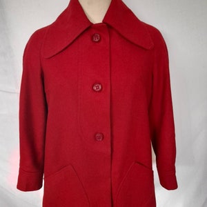 K&ouml;nnte beinhalten: Eine rote Wolljacke mit einem breiten Kragen und vier Kn&ouml;pfen auf der Vorderseite. Die Jacke hat zwei aufgesetzte Taschen auf der Vorderseite.