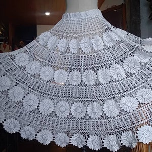 May include: A white crocheted skirt with a floral design. The skirt is full and flowing, and it is made with a delicate crochet stitch.