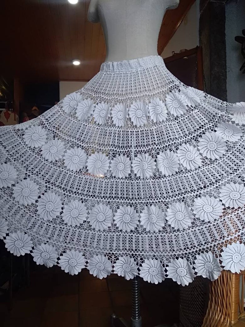 May include: A white crocheted skirt with a floral design. The skirt is full and flowing, and it is made with a delicate crochet stitch.