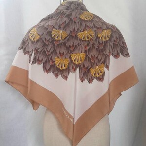 May include: A white silk scarf with a brown and yellow floral design. The scarf has a brown border and the text "ROCHAS - PARIS" is printed in the lower right corner.