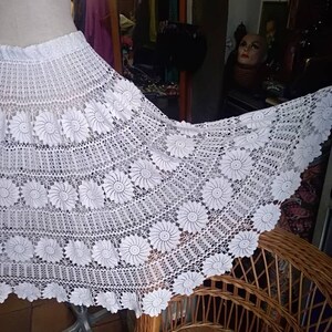 May include: White crochet skirt with a floral design. The skirt is long and flowing, and it has a wide waistband.