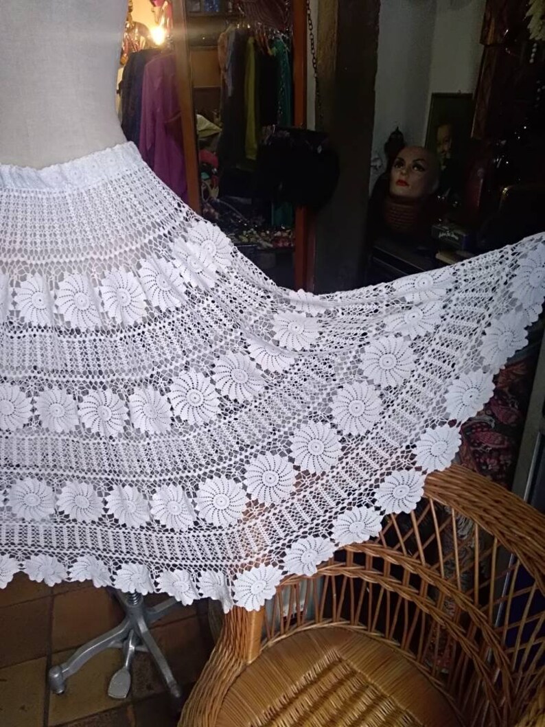 May include: White crochet skirt with a floral design. The skirt is long and flowing, and it has a wide waistband.
