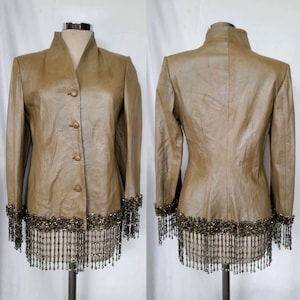 May include: A brown leather jacket with a beaded fringe trim. The jacket has a mandarin collar and a button front closure.