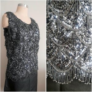 Può includere: Top senza maniche argentato con paillettes e frange di perline. Il top è pesantemente impreziosito da paillettes e perline, creando un effetto scintillante. L'orlo presenta una frangia di perline. Il top è esposto su un manichino.