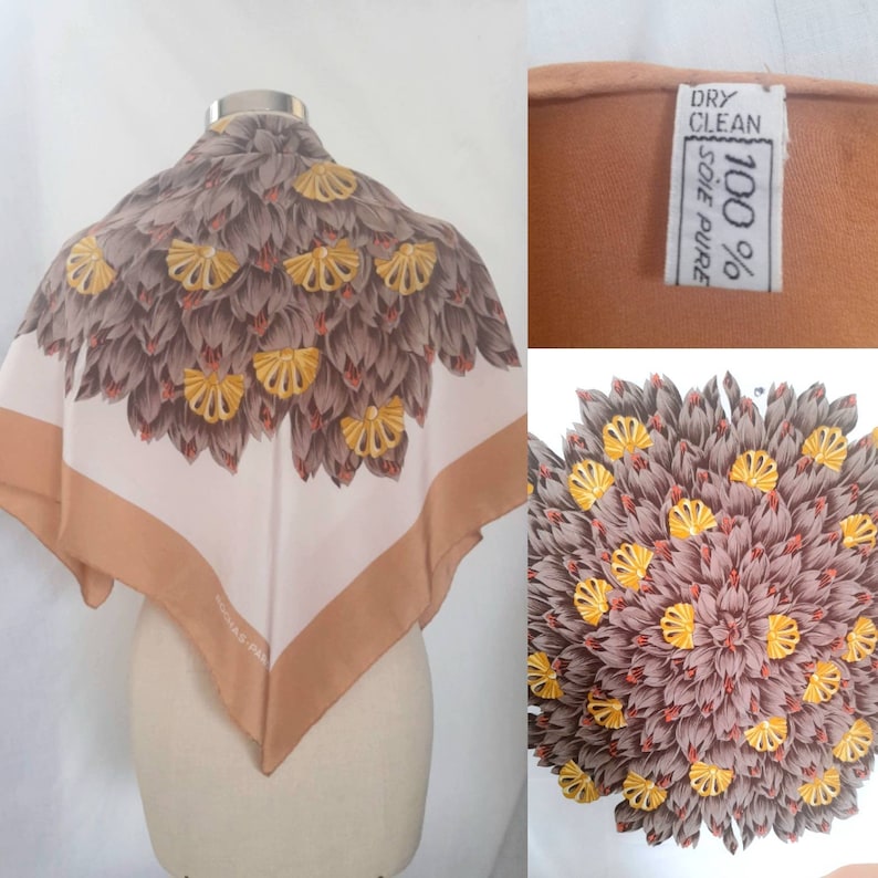 May include: A white silk scarf with a brown and yellow floral pattern. The scarf has a brown border and the text "100% SOIE PURE" is visible on the tag. The tag also says "DRY CLEAN".