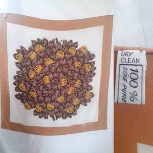 May include: A square silk scarf with a brown and yellow floral design. The scarf has a peach colored border and the text "100% SOIE PURE" and "DRY CLEAN" on a white tag.