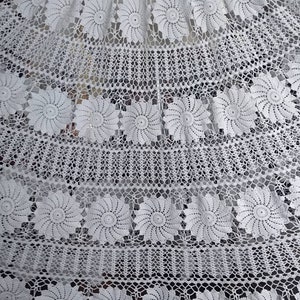 May include: White crocheted tablecloth with a delicate floral pattern. The tablecloth features a repeating design of small, intricate flowers.