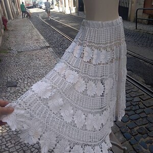 May include: A white crochet skirt with a floral design. The skirt is long and flowing, and it has a delicate lace trim.
